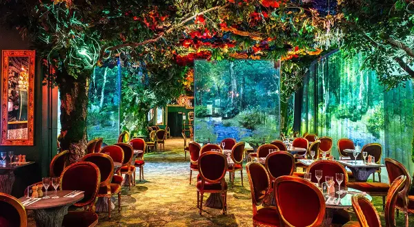 Un restaurant gastronomique féerique, avec des tables dressées sous une voûte de verdure luxuriante et des décors de forêt enchantée.