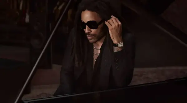 Lenny Kravitz, élégant à Paris, pose près d'un piano, lunettes noires et chaîne argentée.