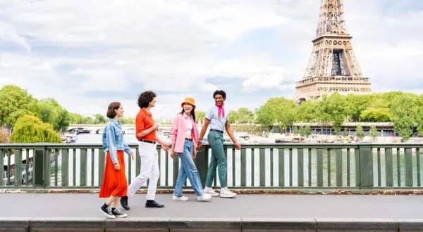 Quatre amis profitent d'une visite insolite Paris gratuit, traversant un pont avec la Tour Eiffel en arrière-plan.