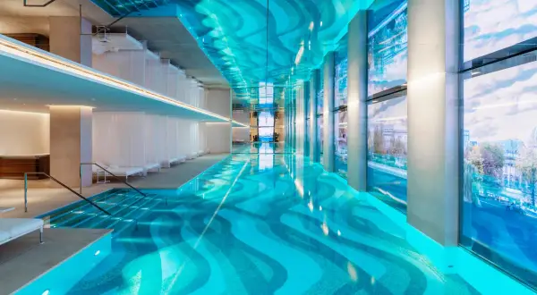 Piscine intérieure luxueuse d'un spa à Paris, avec un éclairage bleu vif, des voilages blancs et une vue sur la ville.