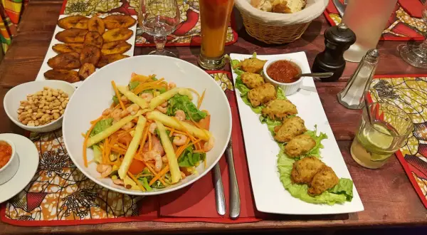 Un festin dans un restaurant antillais : salade de crevettes, accras, bananes plantain frites et un cocktail rafraîchissant.