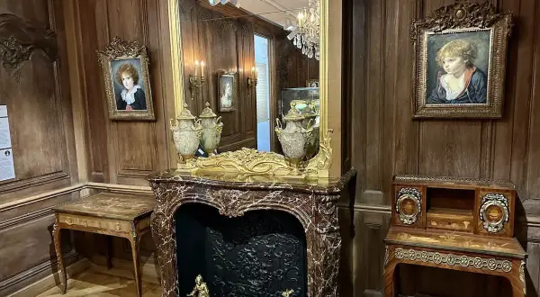 Un salon d'époque avec des portraits d'enfants, une cheminée en marbre et des meubles anciens. On imagine le cognacq jay dégusté dans ce cadre.