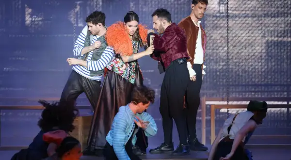Scène de Molière, comédie musicale. Des acteurs costumés, dont une femme à la robe fleurie et un homme en veste bordeaux, jouent sur scène.