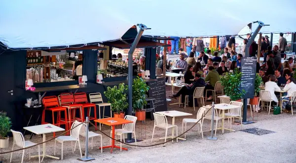 Bar animé sur les quais parisiens, avec des tables et des chaises en terrasse sous une grande tente blanche.