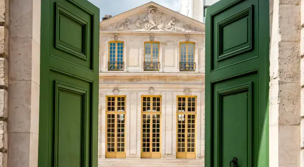 Portes vertes ouvertes sur le pavillon Vendôme à Paris, avec sa façade ornée et ses grandes fenêtres jaunes.