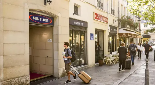 Un jeune homme avec une valise et une carte cherche que faire ce week-end à Paris, passant devant des cafés et l'entrée de la station "MINTURE".