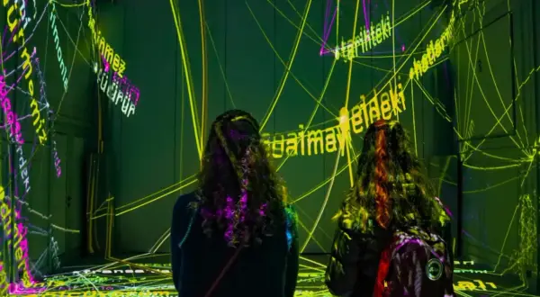 Deux personnes découvrent une exposition immersive à Paris, baignée de lumières vives et de textes projetés.