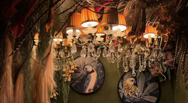 Décor luxuriant et excentrique d'un restaurant insolite à Paris, avec des lustres ornés, des plantes suspendues et des tableaux d'oiseaux exotiques.