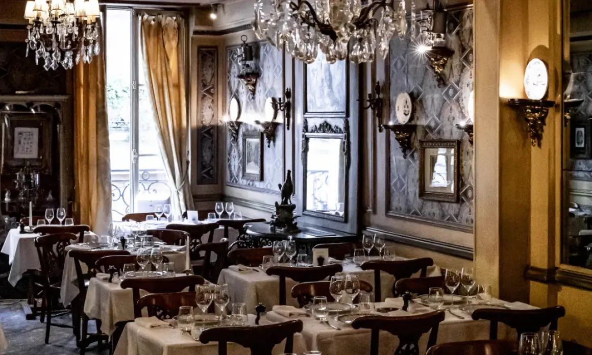Tables dressées dans le plus vieux restaurant de Paris. Lustres en cristal, papier peint orné et vue sur la rue.