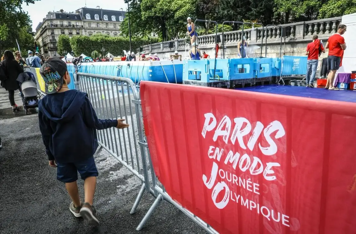 Un enfant observe une piscine temporaire installée pour une journée olympique à Paris. L'inscription "Paris en mode Journée Olympique" est visible sur une banderole rouge.