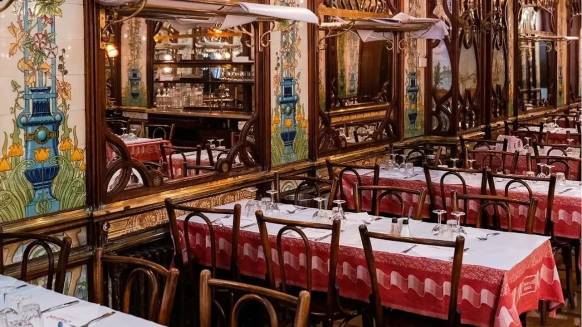Tables dressées dans un bouillon République, décor Art Nouveau avec des carreaux peints et des miroirs.