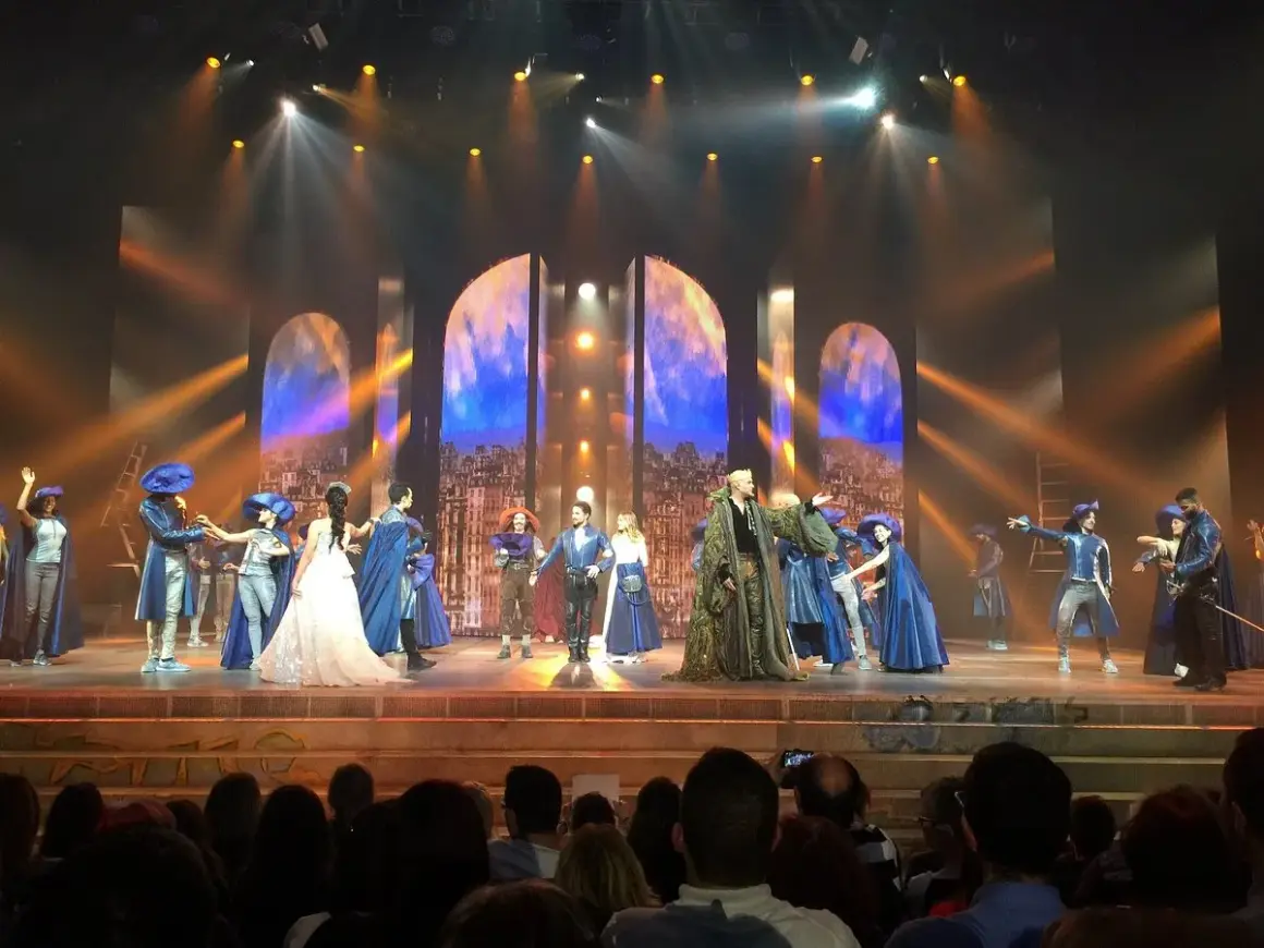 Scène du spectacle "Notre-Dame de Paris" avec des costumes d'époque et un décor évoquant la ville.