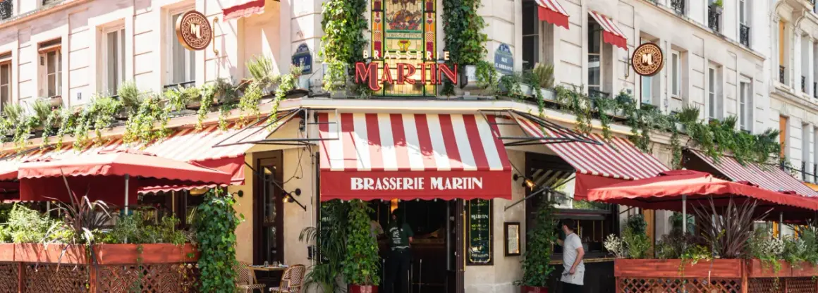 La Brasserie Martin, un coin parisien charmant avec ses auvents rayés rouges et blancs, ses plantes grimpantes et son enseigne lumineuse.