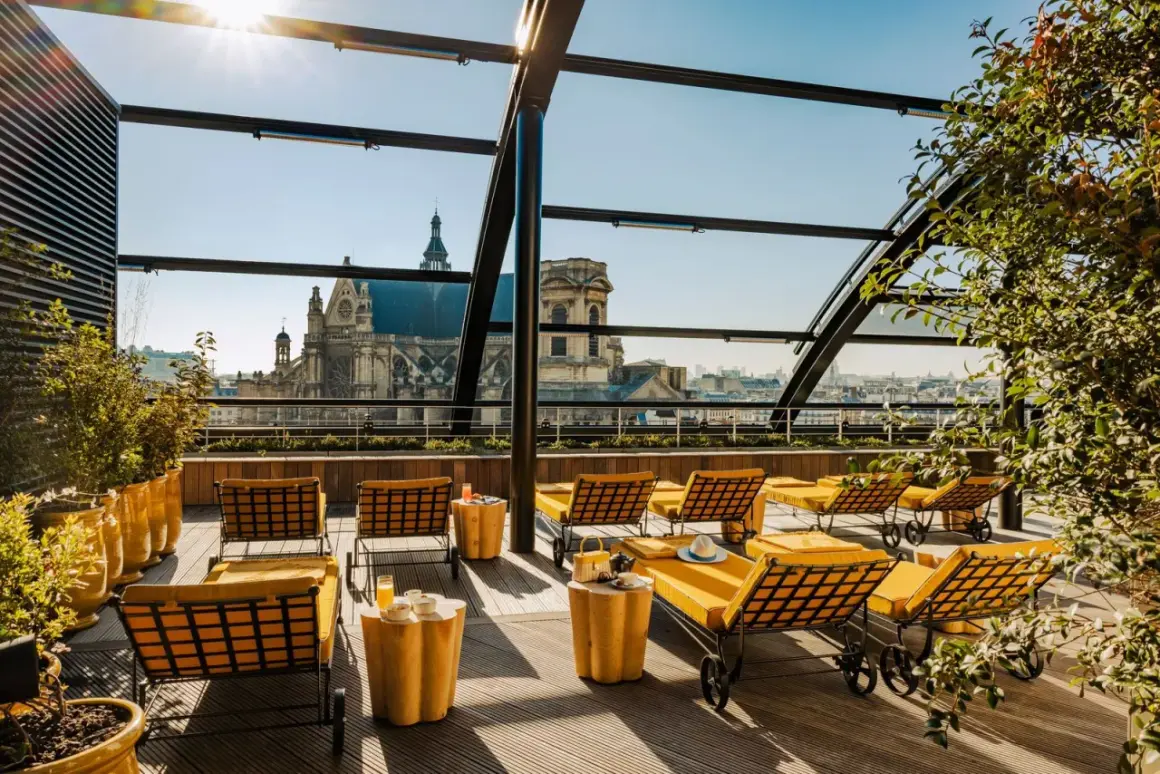 Profitez d'un brunch rooftop à Paris avec vue sur les toits et une église majestueuse. Des chaises longues jaunes invitent à la détente.