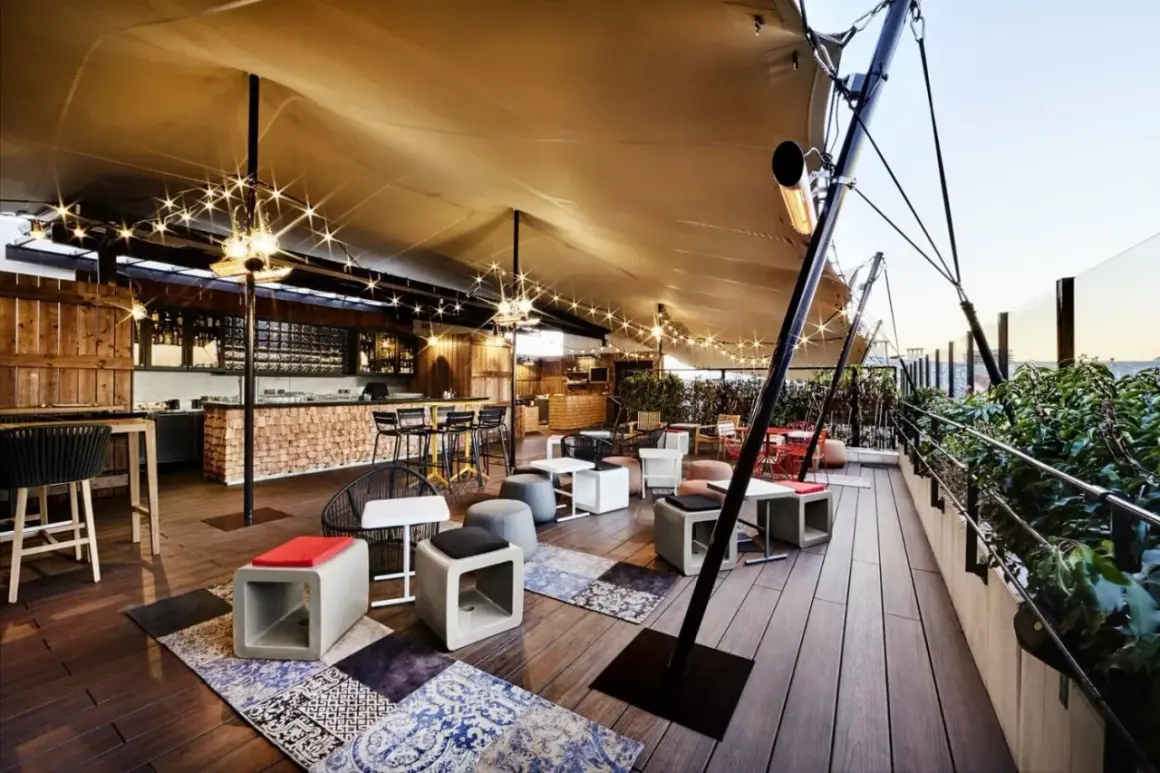 Ambiance chaleureuse sur un rooftop Paris pas cher, avec bar en bois, lumières scintillantes et mobilier cosy. Idéal pour un moment détente.