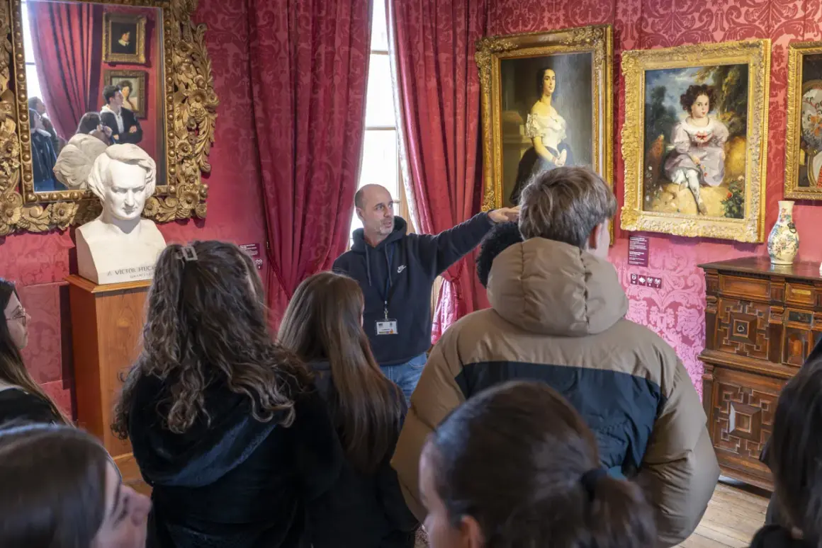 Visite guidée dans la Maison de Victor Hugo à Paris. Un guide montre des tableaux et un buste de l'écrivain à un groupe de visiteurs.