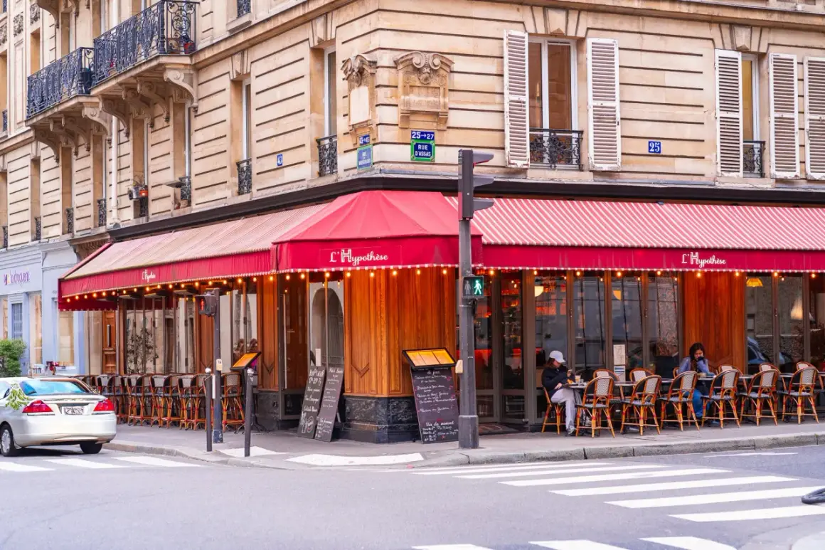 Un café parisien avec des tables en terrasse sous un auvent rouge. L'ambiance d'un food court à Paris.