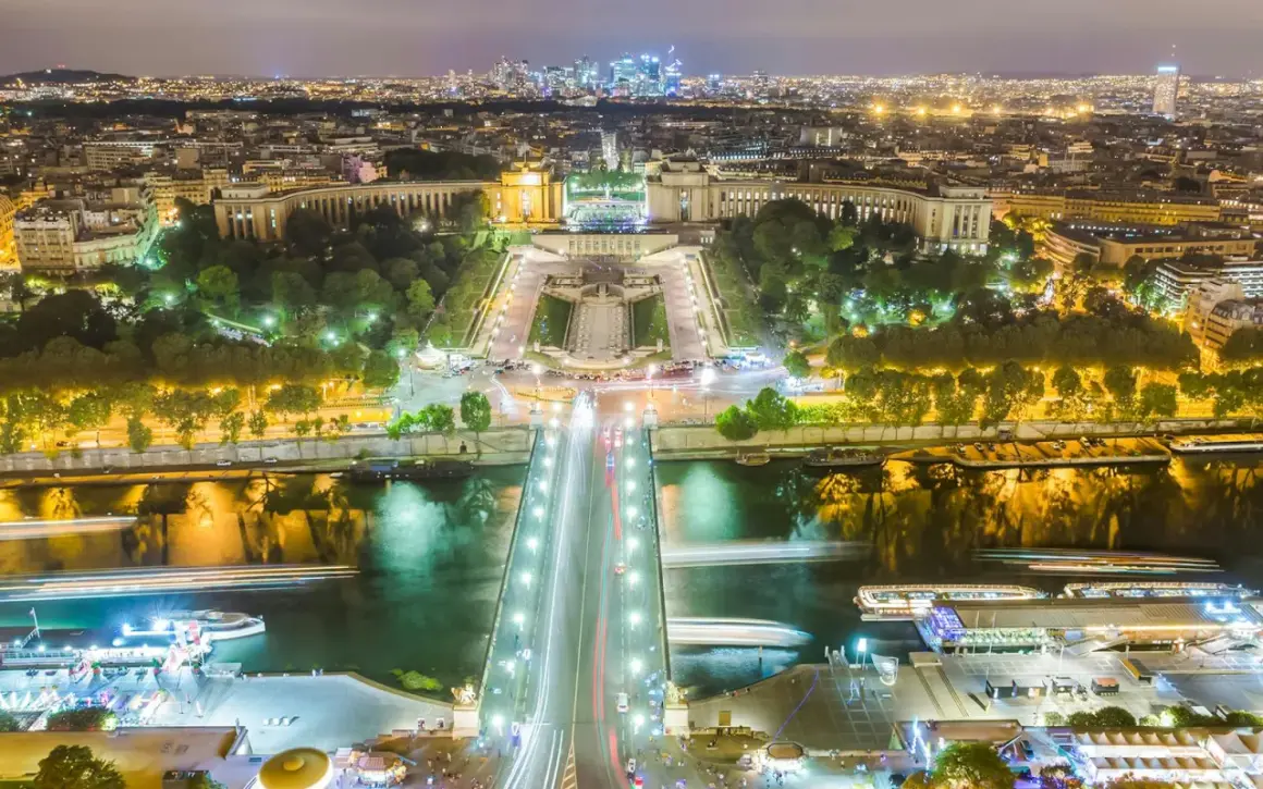 Paris la nuit, le scintillement de la Tour Eiffel se reflète sur la Seine, illuminant la ville.