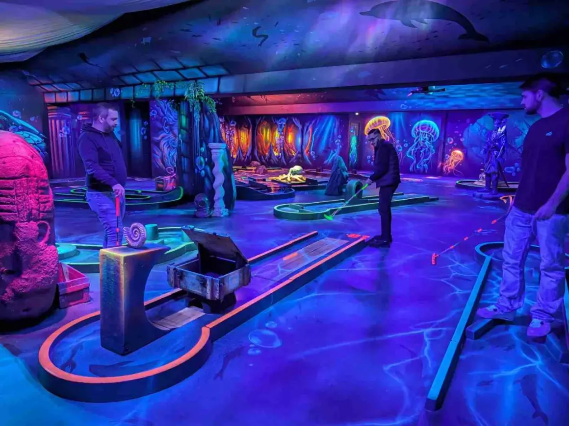 Ambiance sous-marine pour un escape game avec enfant. Parcours de mini-golf fluorescent, décoré de méduses et de dauphins, promettant une aventure ludique.