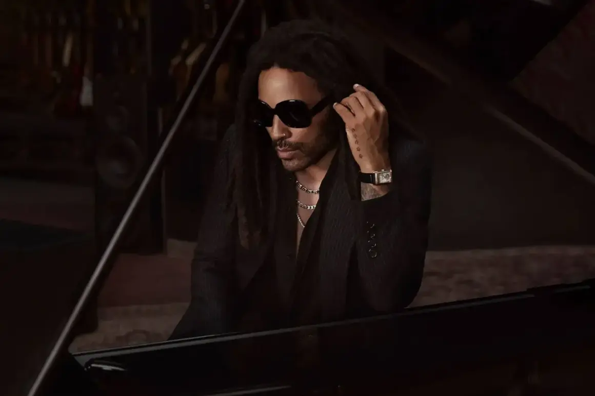 Lenny Kravitz, élégant à Paris, pose près d'un piano, lunettes noires et chaîne argentée.