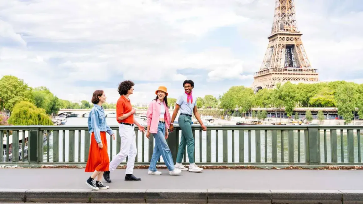 Quatre amis profitent d'une visite insolite Paris gratuit, traversant un pont avec la Tour Eiffel en arrière-plan.