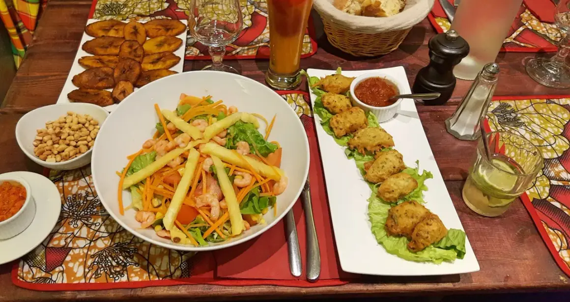 Un festin dans un restaurant antillais : salade de crevettes, accras, bananes plantain frites et un cocktail rafraîchissant.