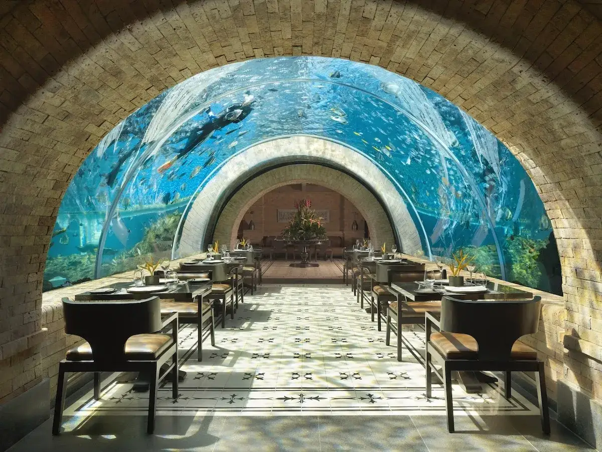 Un restaurant sous la mer, avec des tables dress&eacute;es et un plongeur nageant parmi les poissons dans un tunnel aquatique spectaculaire.