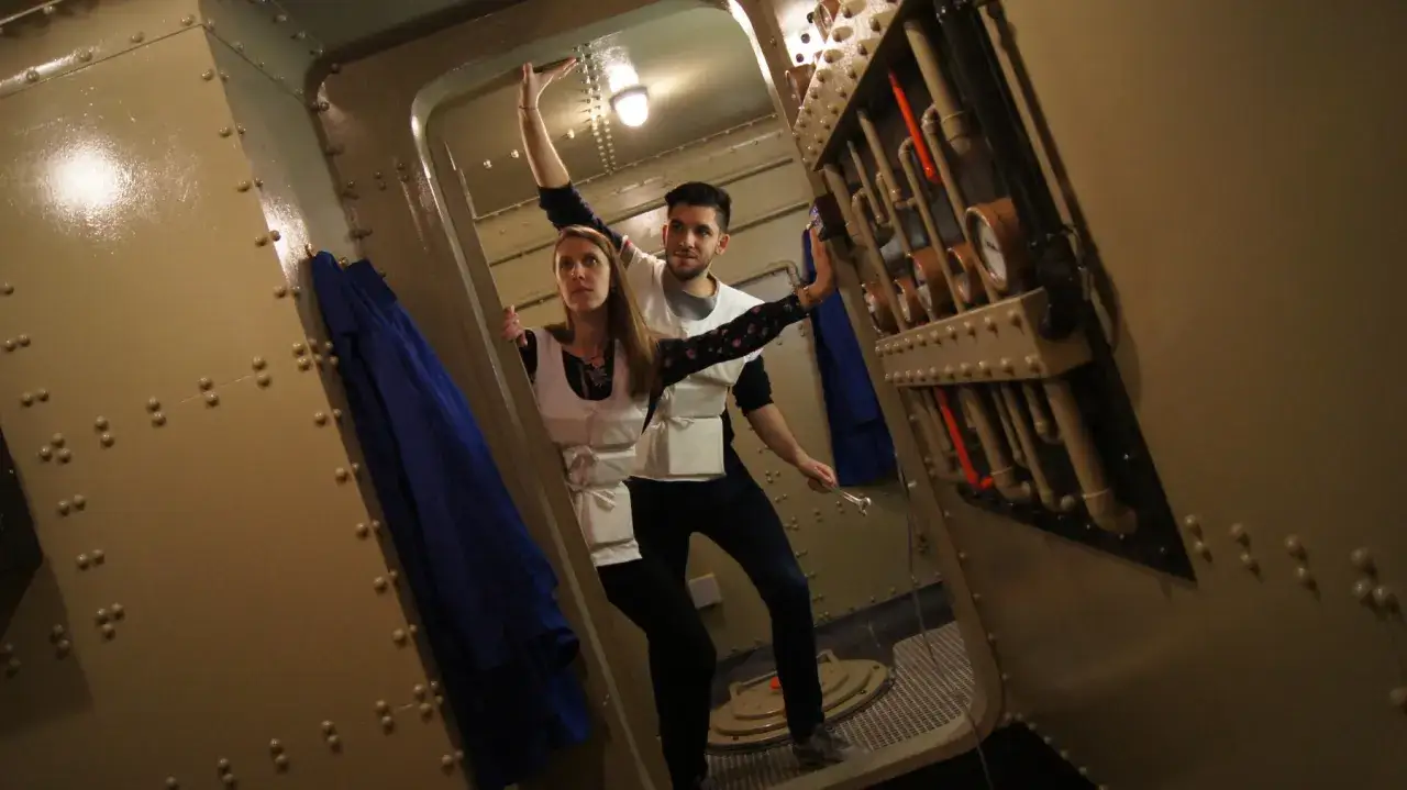 Un couple s'amuse dans un escape game insolite &agrave; Paris, explorant un d&eacute;cor de sous-marin avec des instruments et des tuyaux.