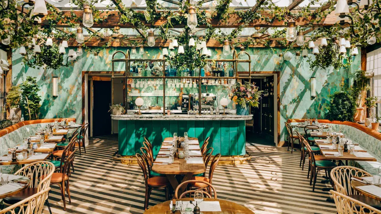 Un &eacute;l&eacute;gant food court &agrave; Paris, avec des tables dress&eacute;es sous une verri&egrave;re luxuriante. Le bar vert &eacute;meraude est le point central de ce lieu chic.