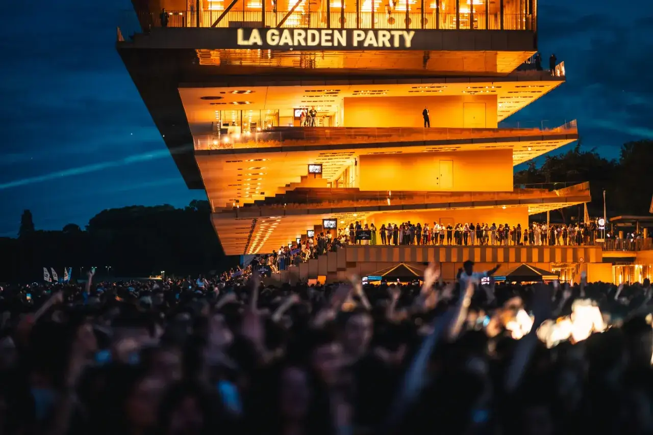 Soir&eacute;e anim&eacute;e &agrave; La Garden Party, ParisLongchamp. Une foule en liesse sous un ciel &eacute;toil&eacute;, illumin&eacute;e par les lumi&egrave;res chaudes du b&acirc;timent.