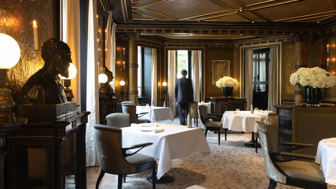 Int&eacute;rieur d'un restaurant gastronomique luxueux, tables dress&eacute;es, buste en bronze, lumi&egrave;res tamis&eacute;es.