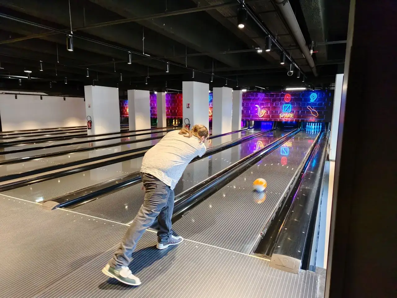 Un joueur lance une boule orange sur une piste de bowling moderne &agrave; Paris. Les sept carr&eacute;s lumineux au fond indiquent les scores.