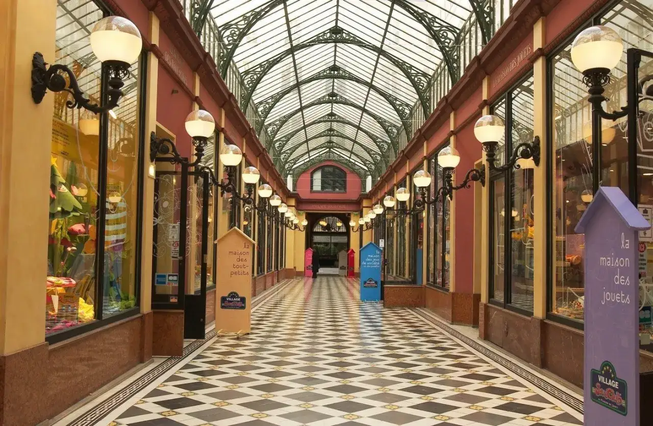 Passage couvert parisien avec sol &agrave; damiers, vitrines de boutiques et verri&egrave;re. Une visite insolite Paris gratuit pour d&eacute;couvrir ce lieu charmant.