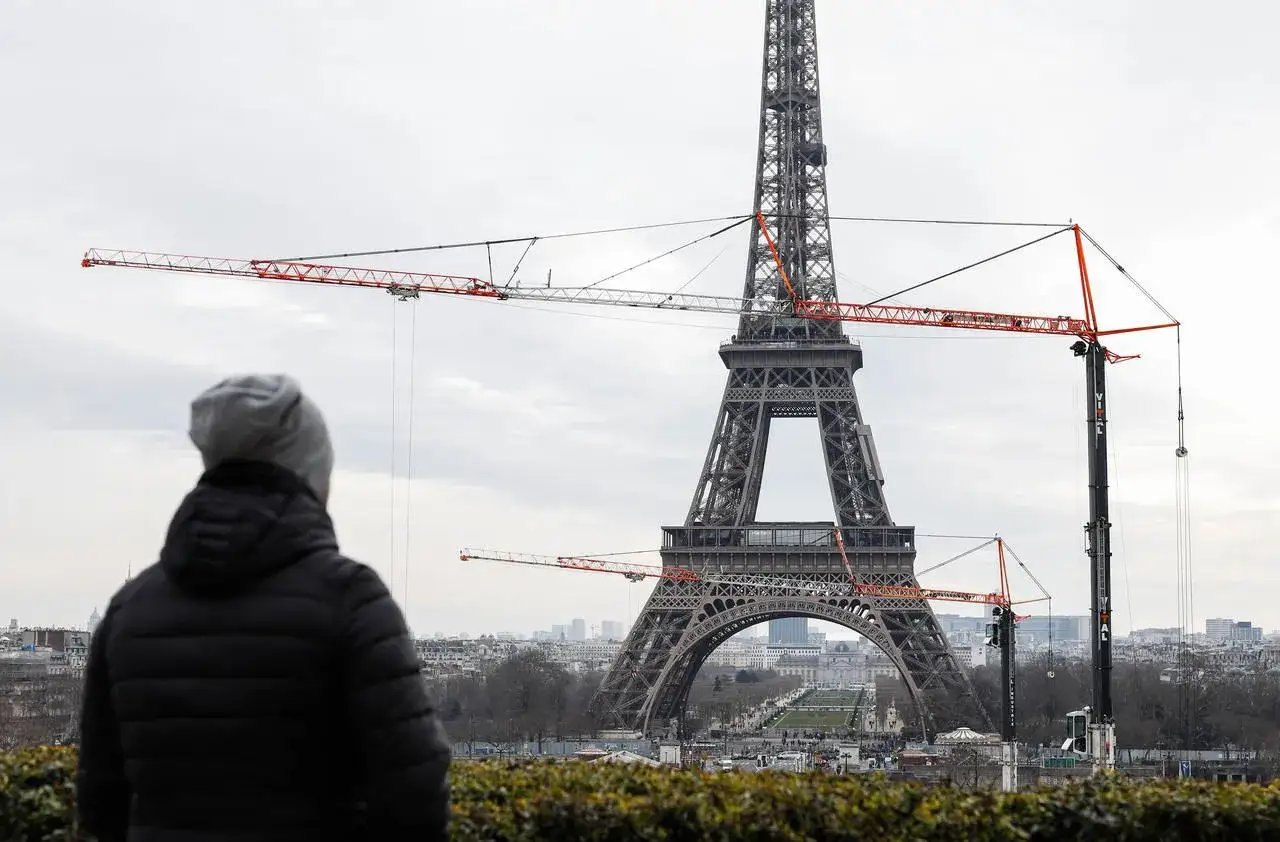Une personne observe la Tour Eiffel, entour&eacute;e de grues. Une sc&egrave;ne inhabituelle pour cette ic&ocirc;ne parisienne, comme une peinture en cours de cr&eacute;ation.