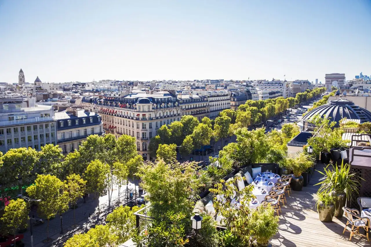 Vue panoramique d'un restaurant sur un toit &agrave; mun paris, avec des tables dress&eacute;es et l'Arc de Triomphe en arri&egrave;re-plan.