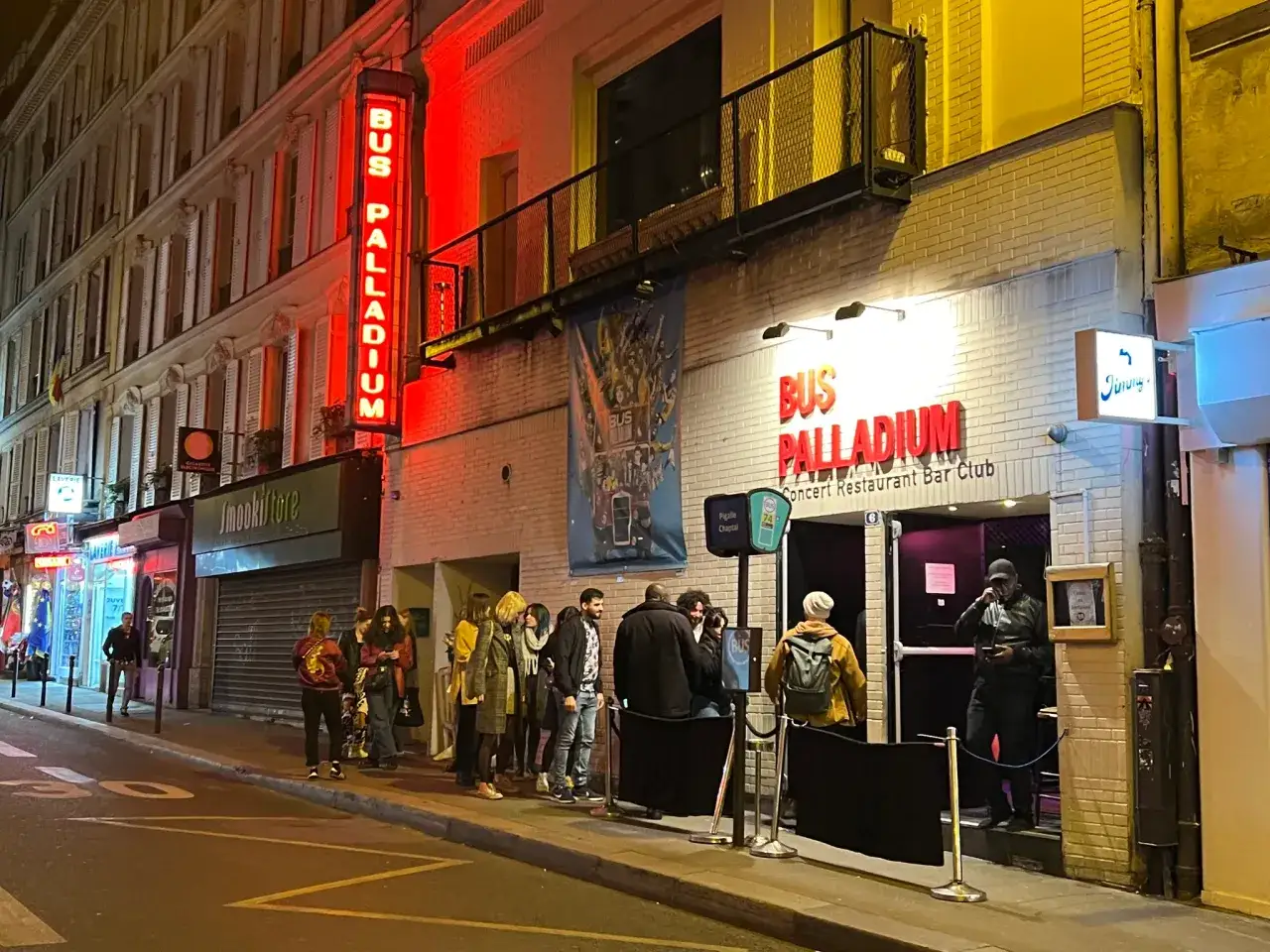 Une foule attend devant le Bus Palladium, un lieu embl&eacute;matique de Paris, illumin&eacute; par des n&eacute;ons rouges.
