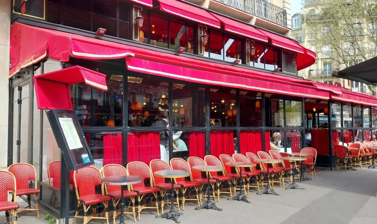 Terrasse d'un restaurant parisien, avec ses chaises rouges et ses tables, sous les auvents rouges. Un menu est visible à l'entrée.