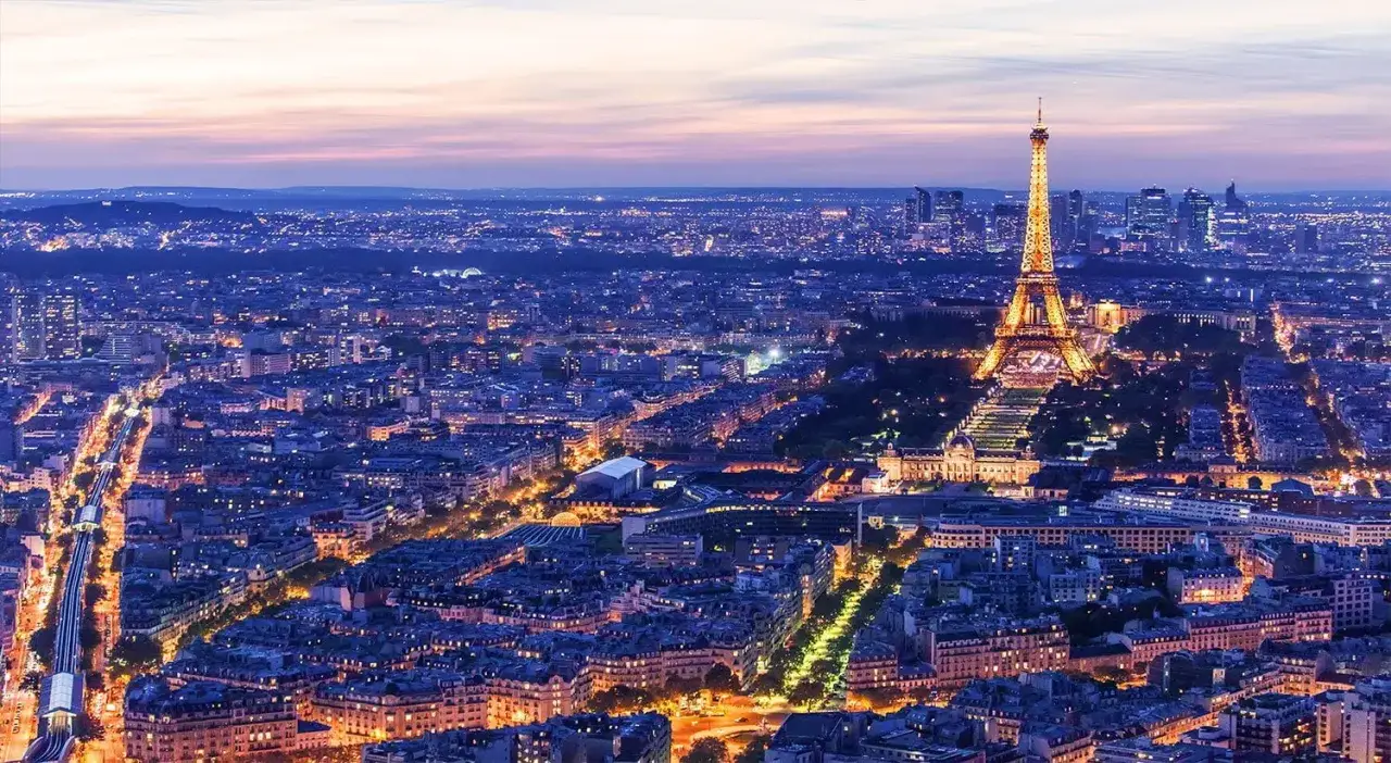 Vue a&eacute;rienne de Paris illumin&eacute; au cr&eacute;puscule, avec la Tour Eiffel scintillante au centre. Un spot photo parisien inoubliable.