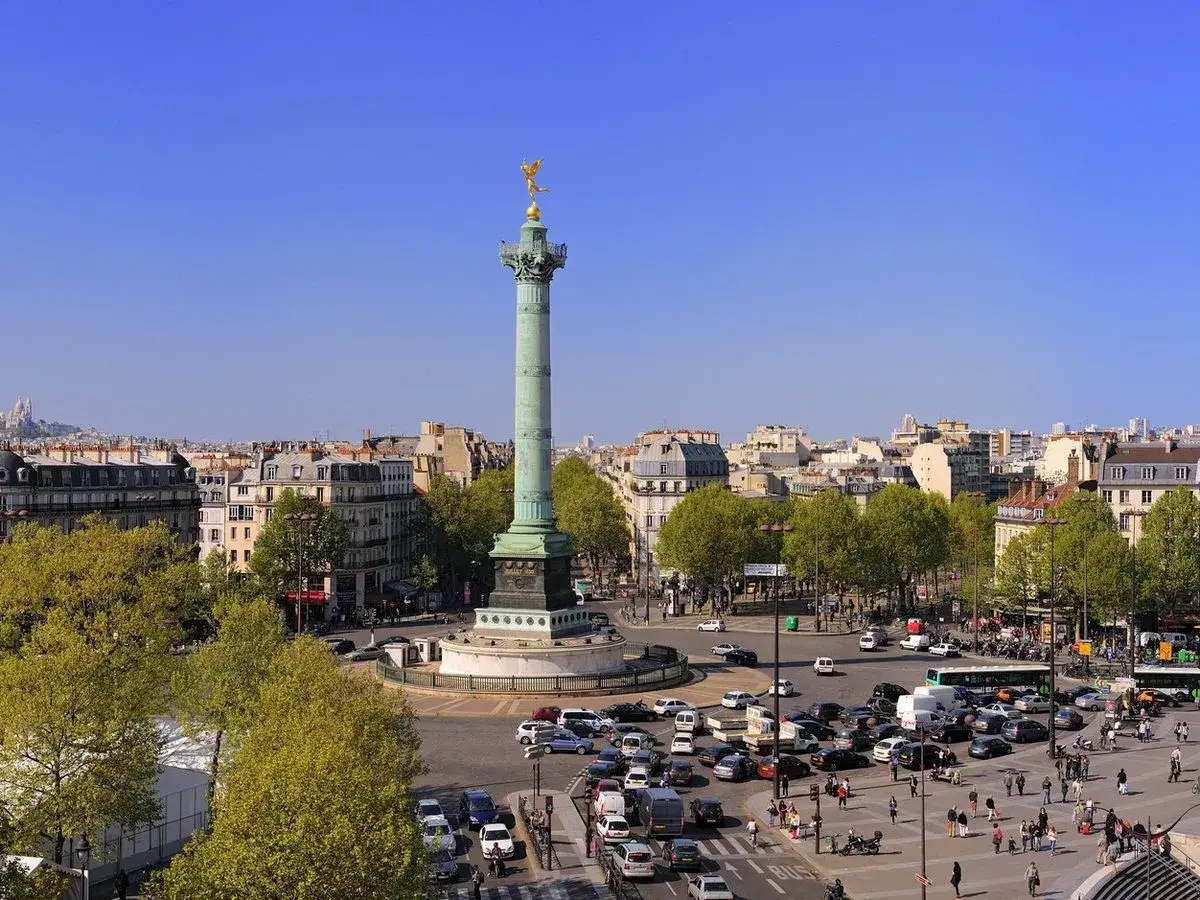 La colonne de Juillet domine la place de la Bastille, anim&eacute;e par le trafic parisien sous un ciel bleu &eacute;clatant.