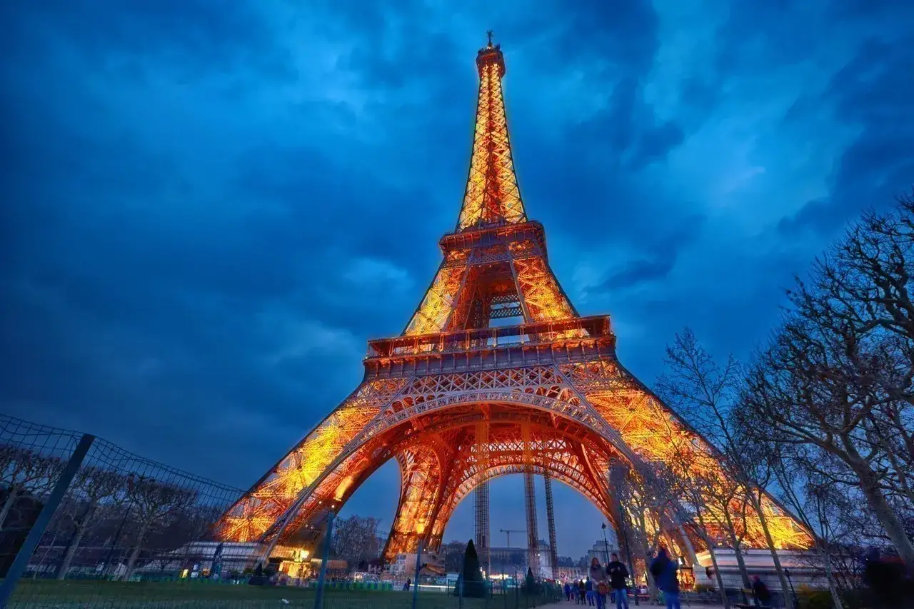 La Tour Eiffel illuminée de nuit, se dresse majestueusement sous un ciel bleu profond, ses lumières chaudes contrastant avec l'obscurité.