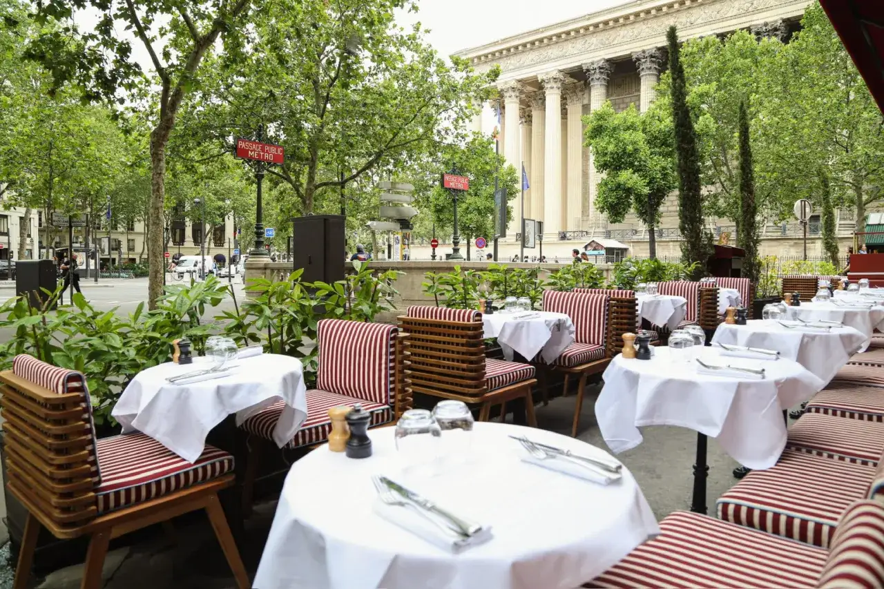 Tables dressées pour un brunch parisien, avec vue sur un bâtiment majestueux et des arbres verdoyants.