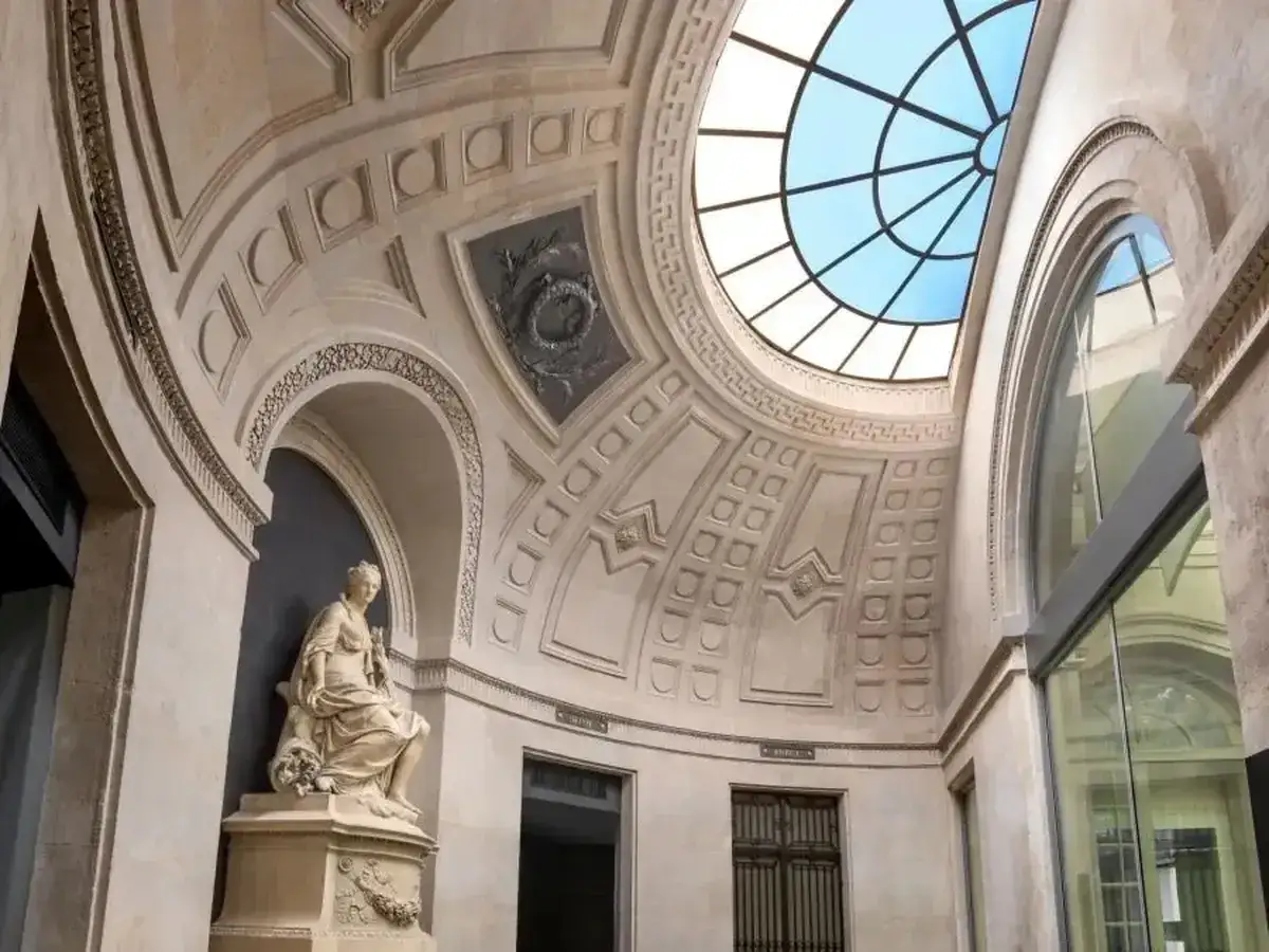 Sculpture dans une cour int&eacute;rieure du mus&eacute;e Monnaie de Paris, sous un d&ocirc;me vitr&eacute;.