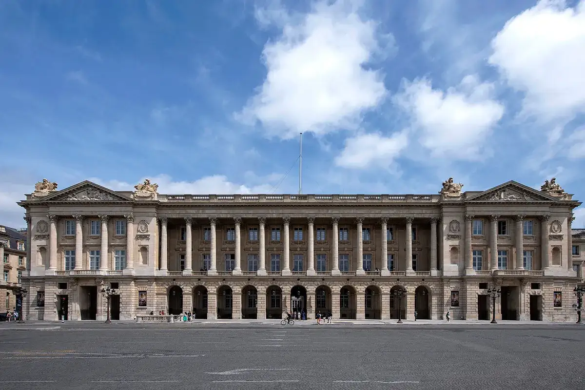 Le majestueux H&ocirc;tel de la Marine &agrave; Paris, avec ses colonnes imposantes et son architecture classique, se dresse sous un ciel bleu parsem&eacute; de nuages.