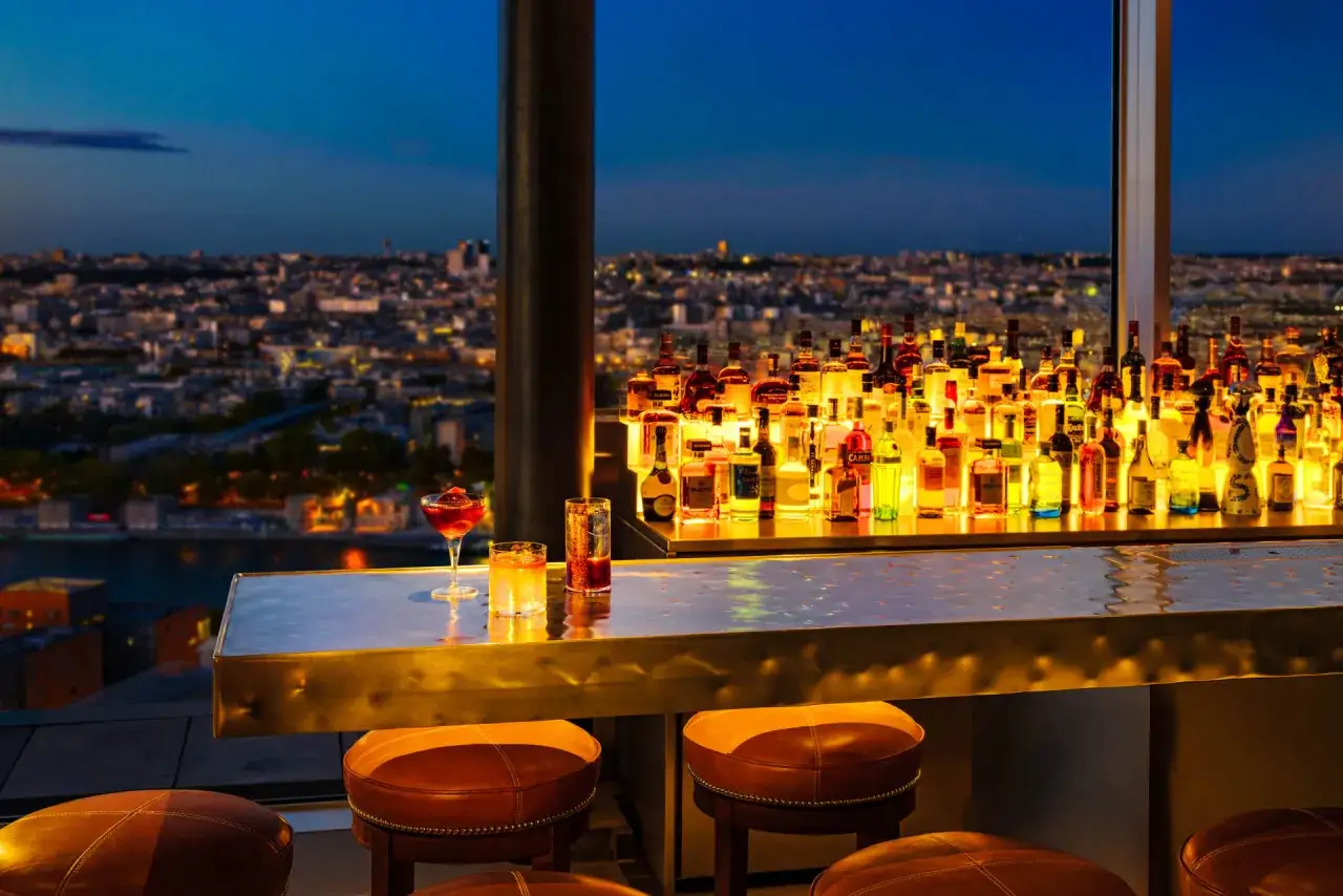 Un bar avec vue panoramique sur Paris au cr&eacute;puscule. Des bouteilles illumin&eacute;es sur le comptoir, un cocktail vous attend au perchoir M&eacute;nilmontant.