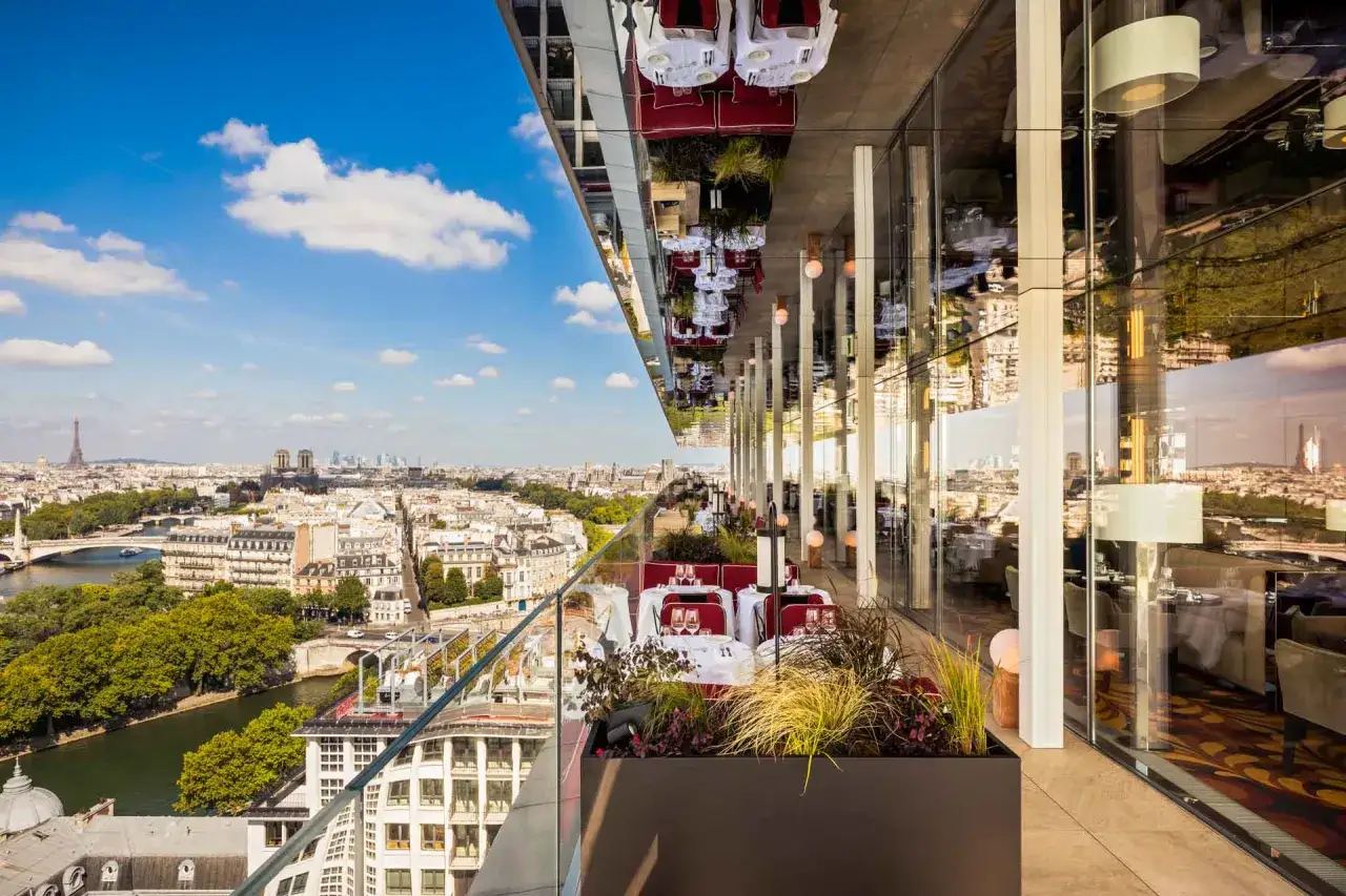 Restaurant avec vue sur la Tour Eiffel. Tables dress&eacute;es sur une terrasse panoramique, reflets de Paris dans le plafond.