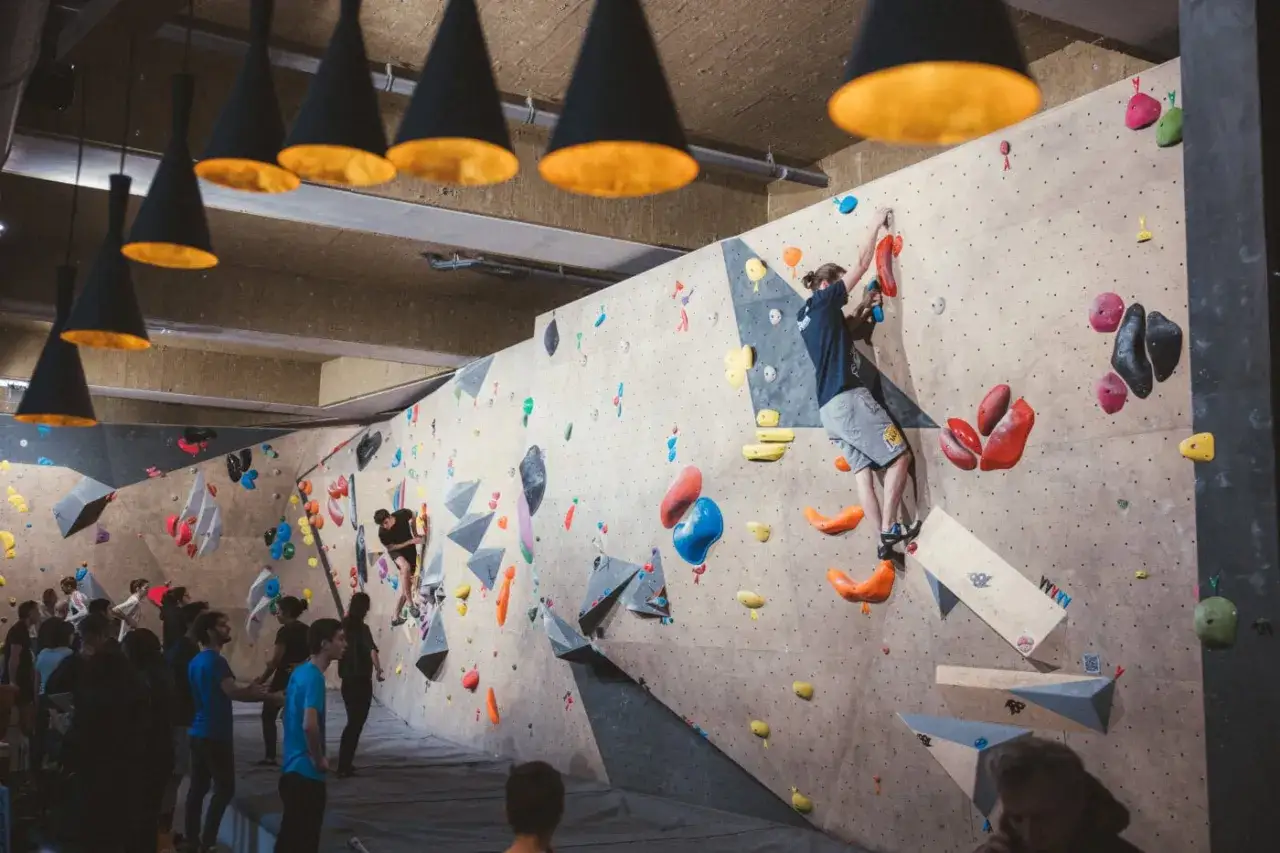 Ambiance conviviale dans le climbing district Batignolles. Des grimpeurs s'exercent sur des murs color&eacute;s, sous des suspensions design.