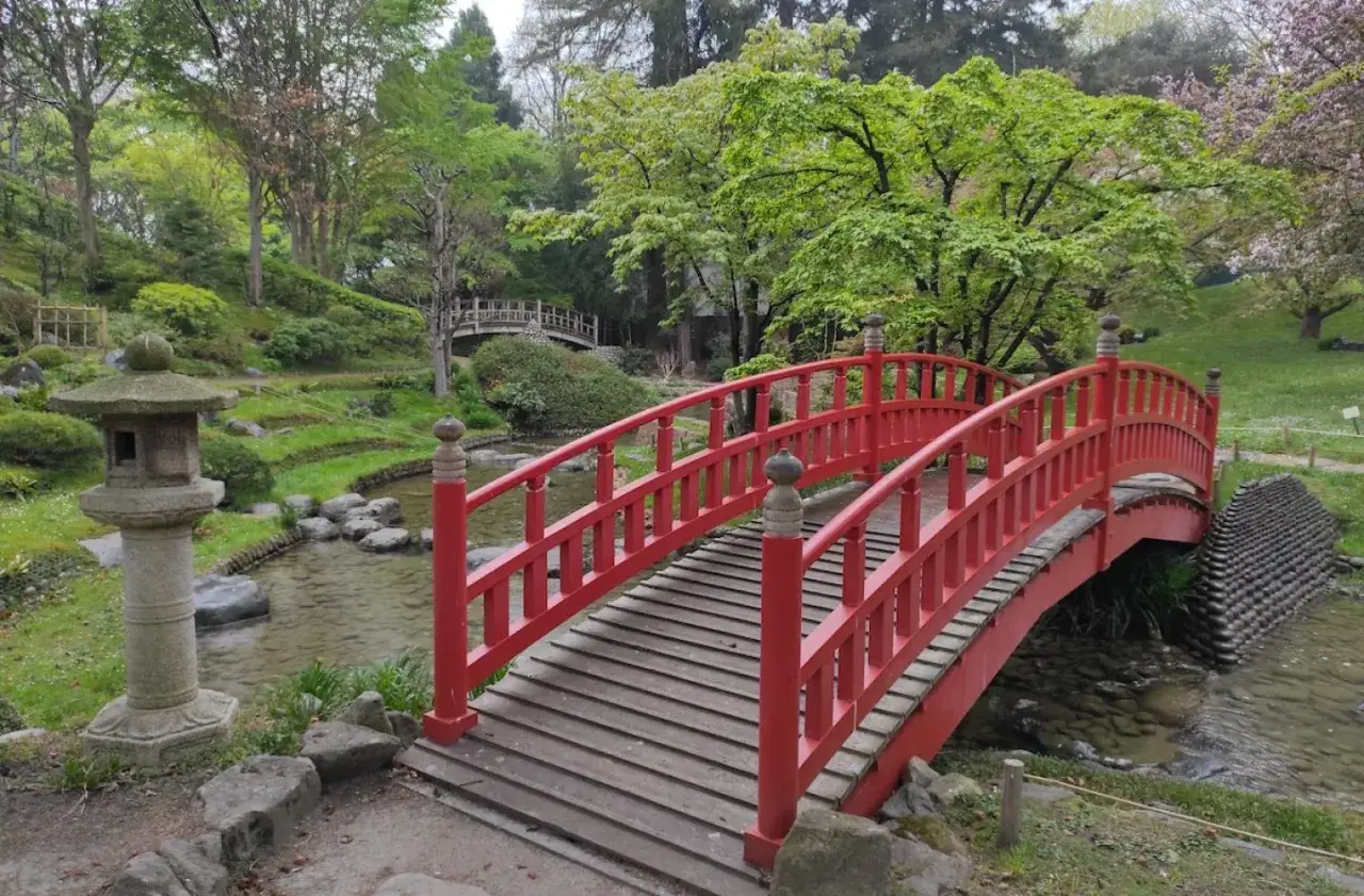 Pont rouge arqu&eacute; dans le jardin japonais du mus&eacute;e d&eacute;partemental Albert-Kahn, avec une lanterne en pierre et un ruisseau.