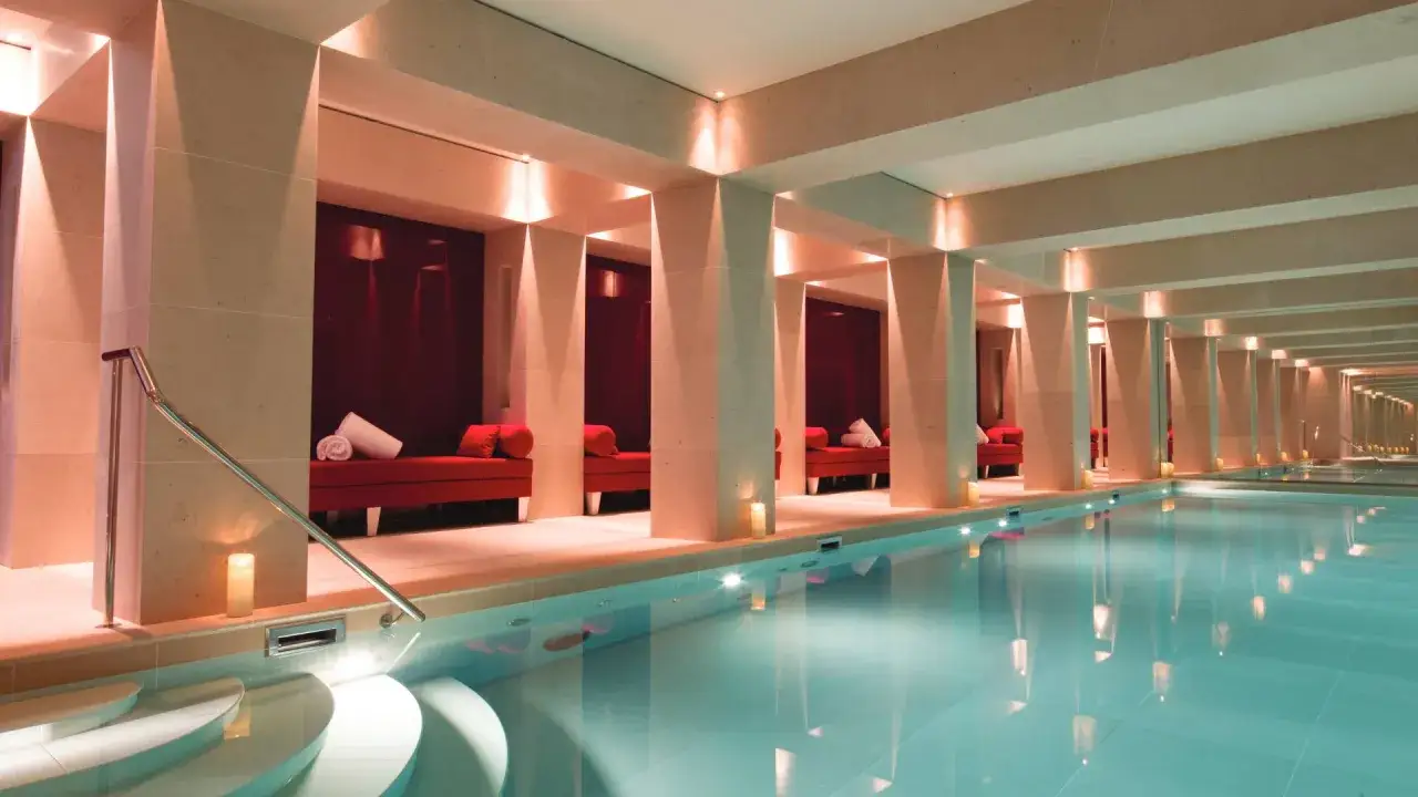 Piscine int&eacute;rieure luxueuse d'un spa &agrave; Paris, avec des banquettes rouges, des bougies et une eau bleut&eacute;e scintillante.