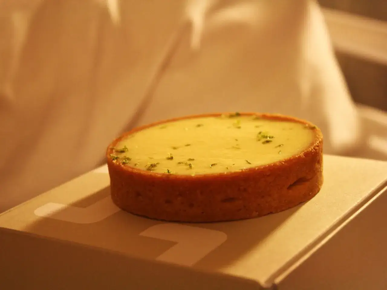 Un d&eacute;licieux dessert parisien, une tartelette citronn&eacute;e aux zestes verts, pos&eacute;e sur un livre blanc.