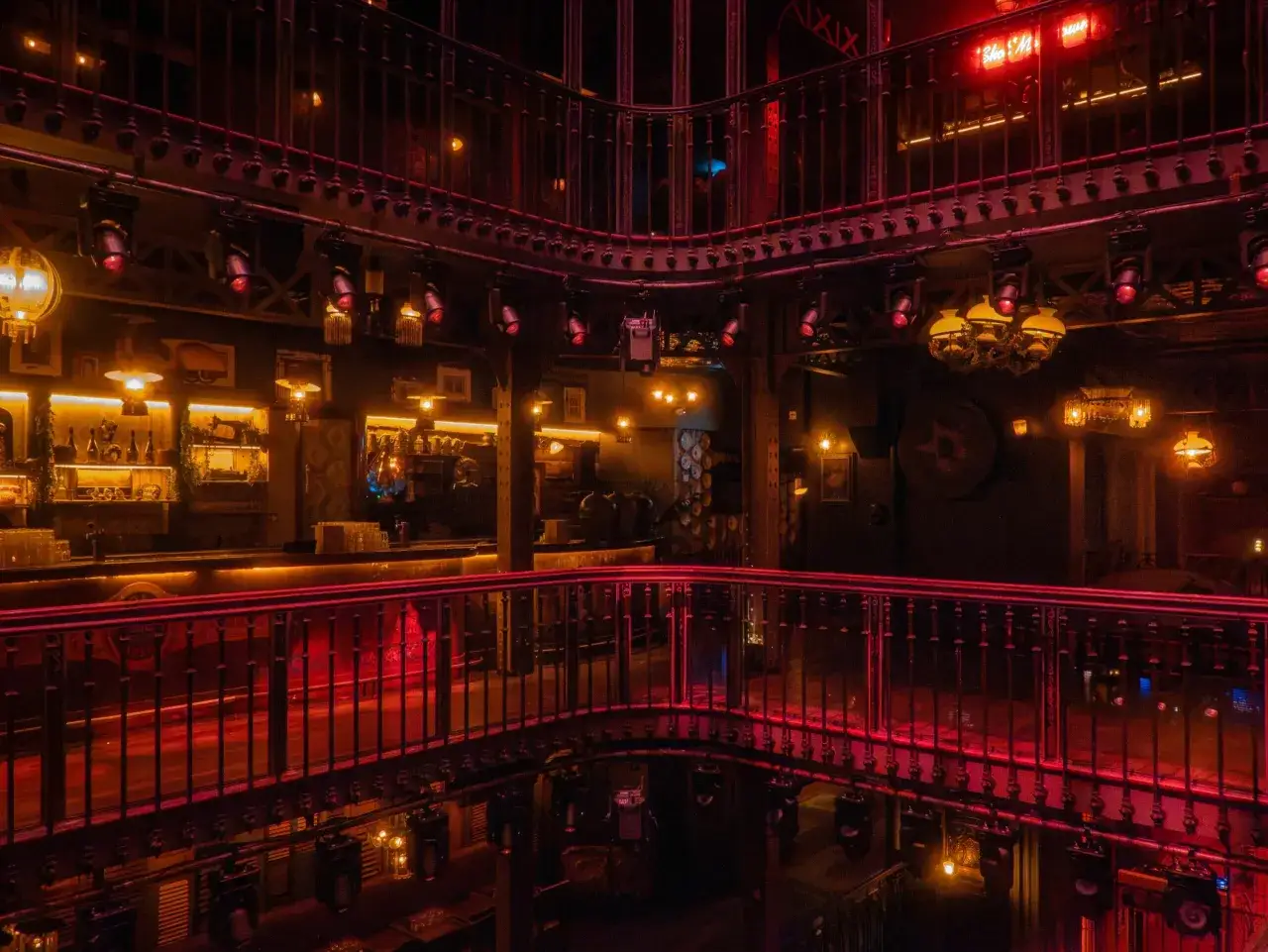L'int&eacute;rieur d'un bar &agrave; l'ambiance festive, &eacute;clair&eacute; par des lumi&egrave;res rouges et dor&eacute;es. On aper&ccedil;oit un bar, des balustrades orn&eacute;es et des lustres, &eacute;voquant un barrio latino &agrave; Paris.
